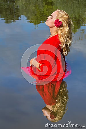 Blonde woman in red stands in natural water Stock Photo