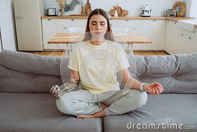 Blonde woman with stylish prosthesis arm meditates on sofa Stock Photo