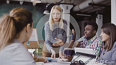 Blonde woman team leader giving direction to mixed race team of young guys. Creative business meeting at modern office. Stock Photo