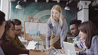 Blonde woman team leader giving direction to mixed race team of young guys. Creative business meeting at modern office. Stock Photo