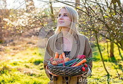 Blonde woman with vegetables in basket in blooming garden Stock Photo