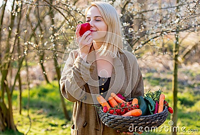 Blonde woman with vegetables in basket in blooming garden Stock Photo