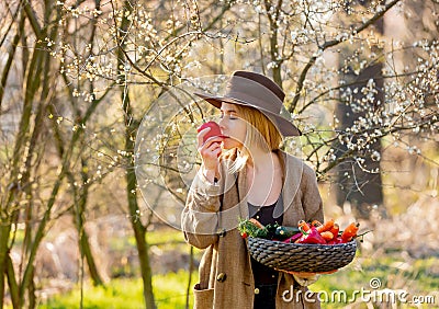 Blonde woman with vegetables in basket in blooming garden Stock Photo