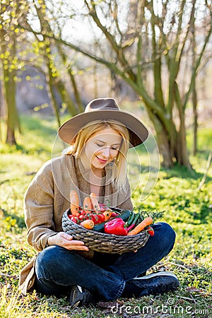 Blonde woman with vegetables in basket in blooming garden Stock Photo