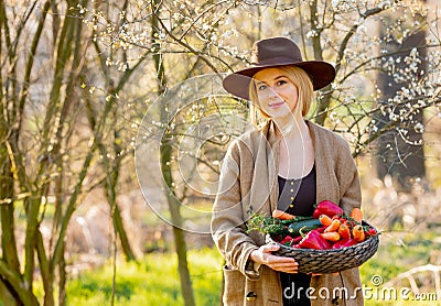 Blonde woman with vegetables in basket in blooming garden Stock Photo