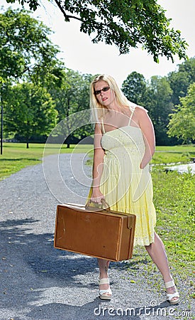 Blonde woman waits by road with suitcase Stock Photo