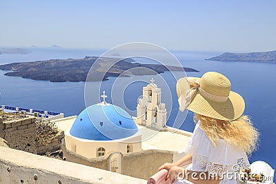 Blonde woman watching view of Santorini near three bells of Fira church in Fira, Santorini, Greece Stock Photo