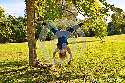 Blonde woman and young gymnast acrobat athlete performing aerial exercise on air ring outdoors in park. Lithe woman in blue Stock Photo