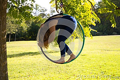 Blonde woman and young gymnast acrobat athlete performing aerial exercise on air ring outdoors in park. Lithe woman in blue Stock Photo