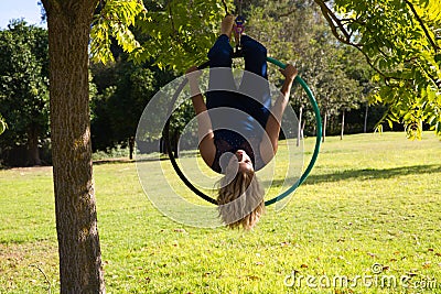 Blonde woman and young gymnast acrobat athlete performing aerial exercise on air ring outdoors in park. Lithe woman in blue Stock Photo