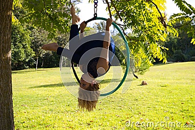 Blonde woman and young gymnast acrobat athlete performing aerial exercise on air ring outdoors in park. Lithe woman in blue Stock Photo
