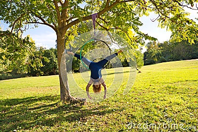 Blonde woman and young gymnast acrobat athlete performing aerial exercise on air ring outdoors in park. Lithe woman in blue Stock Photo