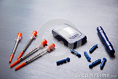 Blood glucose meter, needles and several insulin syringes on a gray wooden table, flat lay Stock Photo