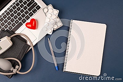 blood pressure meter on laptop with red heart, and pills on dark blue background.paper nootebook with copy space Stock Photo