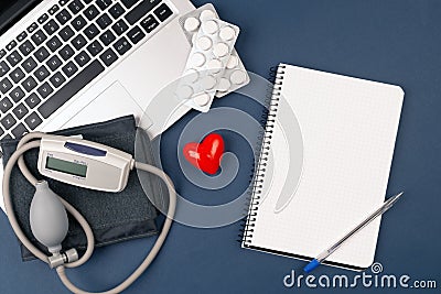 blood pressure meter on laptop with red heart and pills on dark blue background.paper nootebook Stock Photo