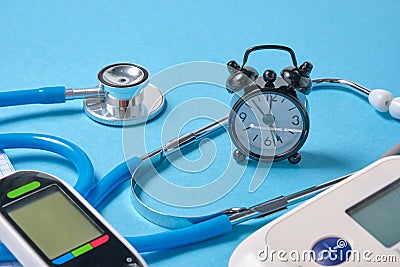 Blood pressure monitor, glucometer, stethoscope, notepad and alarm clock on blue background Stock Photo