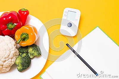 blood pressure monitor on a yellow background, a notebook and a white large plate with vegetables Stock Photo