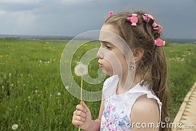 A girl blows on a dandelion against a stormy sky Stock Photo