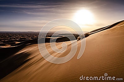 Blowing sand on top of a large sand dune in desert landscape. Early morning sunrise over the desert of Erg Chebbi. Silhouette. Stock Photo