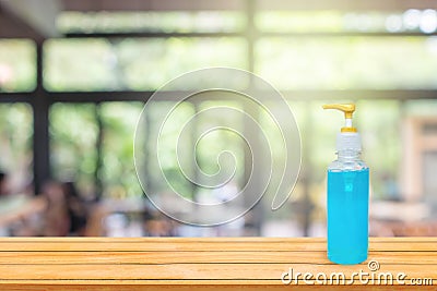 Blue alcohol gel in pump clear bottle put on wooden table with blurry image of coffee shop or cafe restaurant in background. Stock Photo