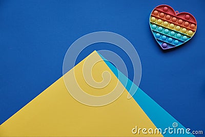 On blue background, multi-colored silicone anti-stress toy in tshape of heart and a pyramid, mountain of yellow-blue Stock Photo