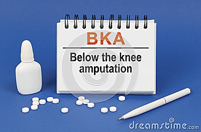 On a blue background, a pen, tablets and a notepad with the inscription - BKA Below the knee amputation Stock Photo