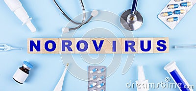 On a blue background, a stethoscope, a thermometer, other medicines and wooden cubes with the text NOROVIRUS. View from above. Stock Photo