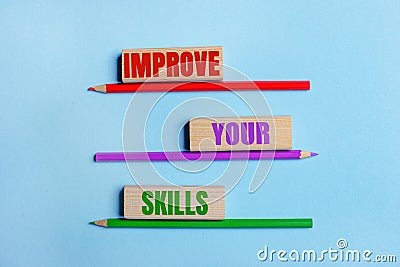 On a blue background, three colored pencils, three wooden blocks with text IMPROVE YOUR SKILLS Stock Photo