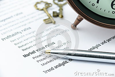 Blue ballpoint pen on a financial ratios analysis check lists with an antique clock and two vintage brass keys. Stock Photo