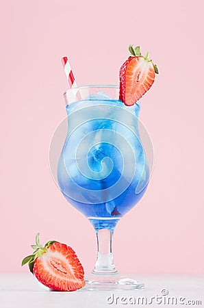 Blue beach cold alcohol drink with curacao liquor, ice cubes, strawberry in elegant wineglass on pastel pink background. Stock Photo