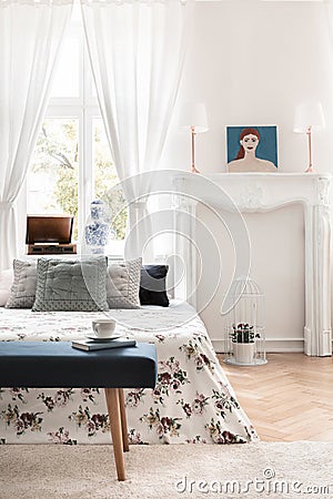 Green bench in front of patterned bed with pillows in white bedroom interior with poster. Real photo Stock Photo
