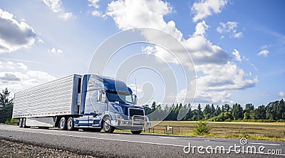 Blue big rig semi truck with grille guard trabsporting frozen cargo in refrigerator semi trailer with skirt spoiler running on the Stock Photo