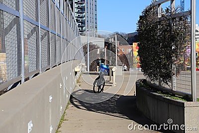 A blue bike parked on a sidewalk on a freeway overpass surrounded by office buildings and blue sky Editorial Stock Photo