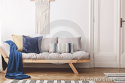 Blue blanket and cushions on beige wooden sofa in white loft interior with door. Real photo Stock Photo