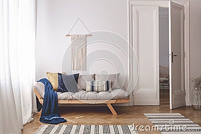 Blue blanket and pillows on wooden couch in white living room interior with rugs and door. Real photo Stock Photo