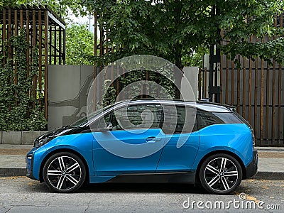 Blue BMW i3 stands near the sidewalk against the background of green trees Stock Photo