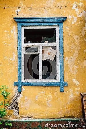 Blue broken window in old yellow abandoned house Stock Photo