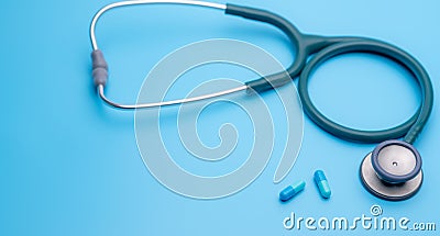 Blue capsule pills and green stethoscope on blue background. Health checkup. Cardiology doctor equipment for heartbeat test. Stock Photo