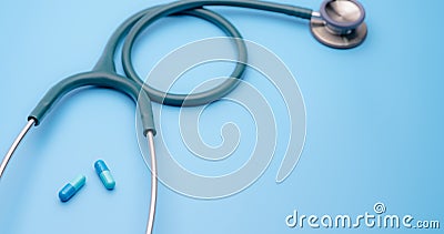 Blue capsule pills and green stethoscope on blue background. Health checkup. Cardiology doctor equipment for heartbeat test. Stock Photo