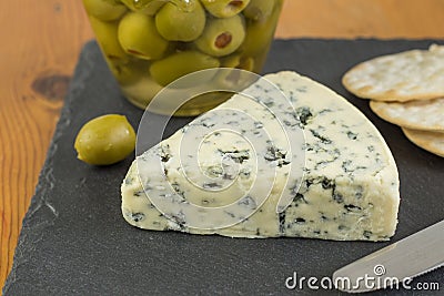 Blue cheese wedge with defocused jar of green olives and cracker Stock Photo