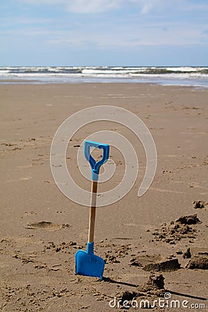 Blue childs spade on the beach with sea in the distance Stock Photo