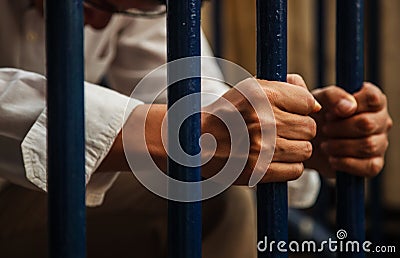 A blue collar man wearing white shirt and brown slacks behind the iron fence, hand holding iron fence with a sense of hopelessness Stock Photo