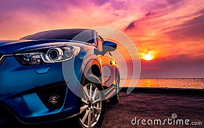 Blue compact SUV car with sport and modern design parked on concrete road by the sea at sunset. Environmentally friendly Stock Photo