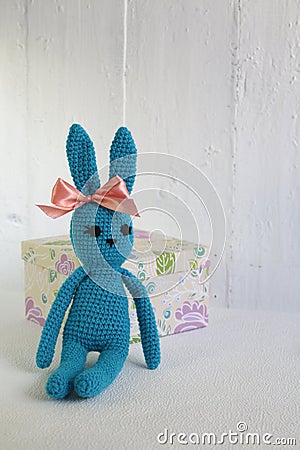 A blue crocheted banny rabbit sits near a gift box on a white background Stock Photo