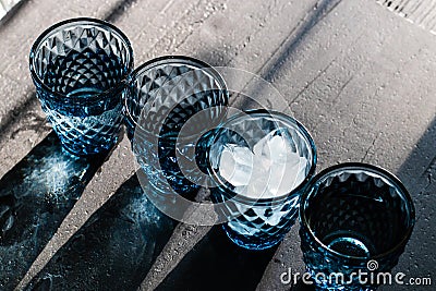 Blue crystal glasses of geometric pattern with ice and drinks in diagonal line and giving colorful shadows on black top Stock Photo