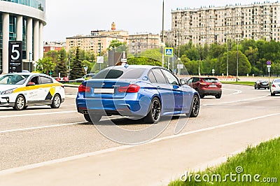 Blue 320d sedan F30 car moving on the street. Rear side view of BMW 3 Series auto driving on the road with city background Editorial Stock Photo