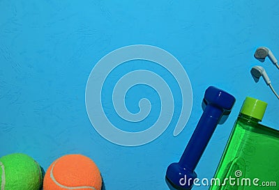 Blue dumbbell, Green tennis ball, earphone and bottle indicating workout plan on blue background. Stock Photo