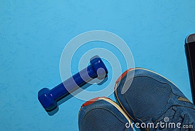 Blue dumbbell, sneakers and smartphone indicating workout plan on blue background Stock Photo