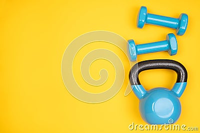 Blue dumbbells and a kettlebell on yellow background Stock Photo