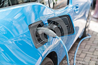 Blue electric car recharging on street with charge cable and plug leading to charge point. Stock Photo